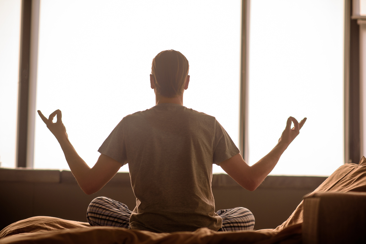 Man Meditating on Bed Facing Open Window